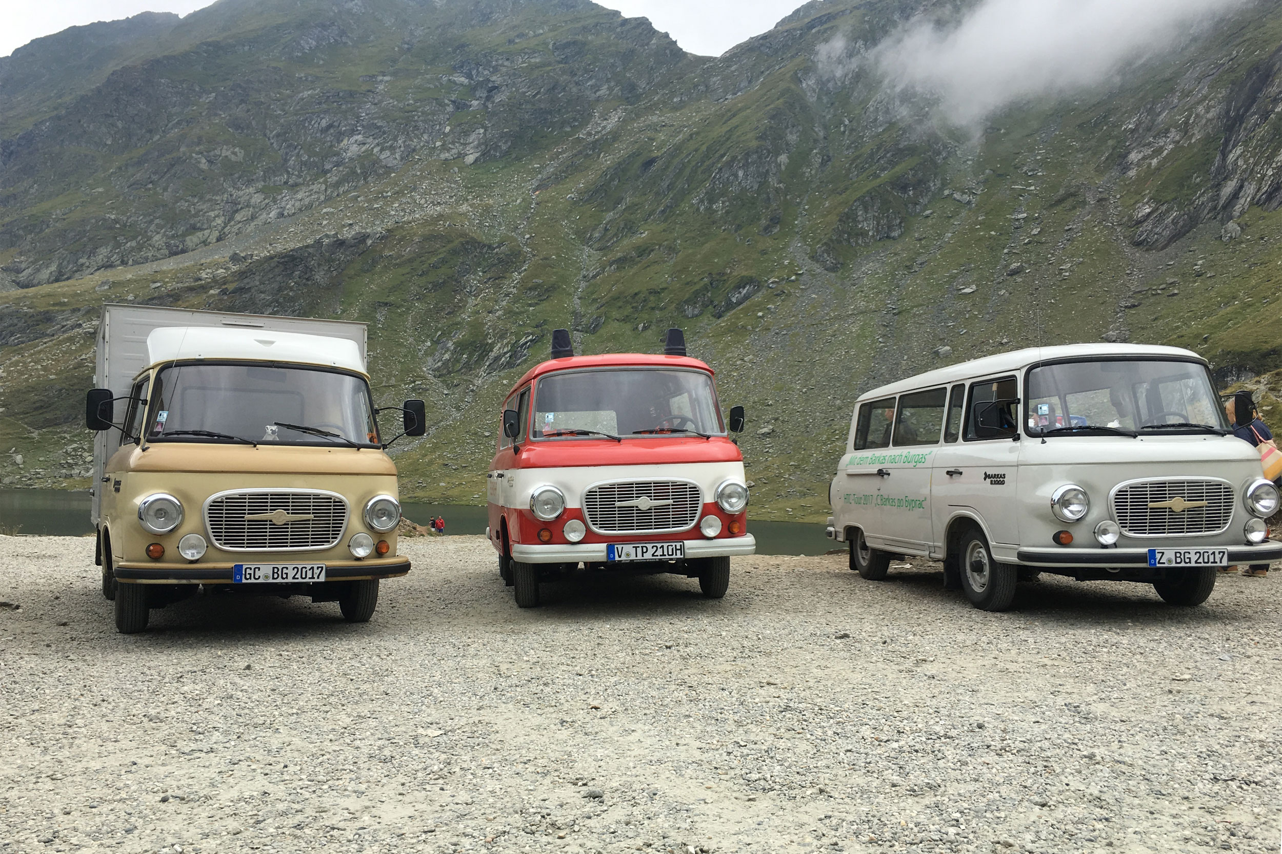 Mit dem Barkas nach Burgas – Oldtimermuseums Culitzsch Drei Barkas-Fahrzeuge auf einem Parkplatz vor einem Gebirgssee in Bulgarien.