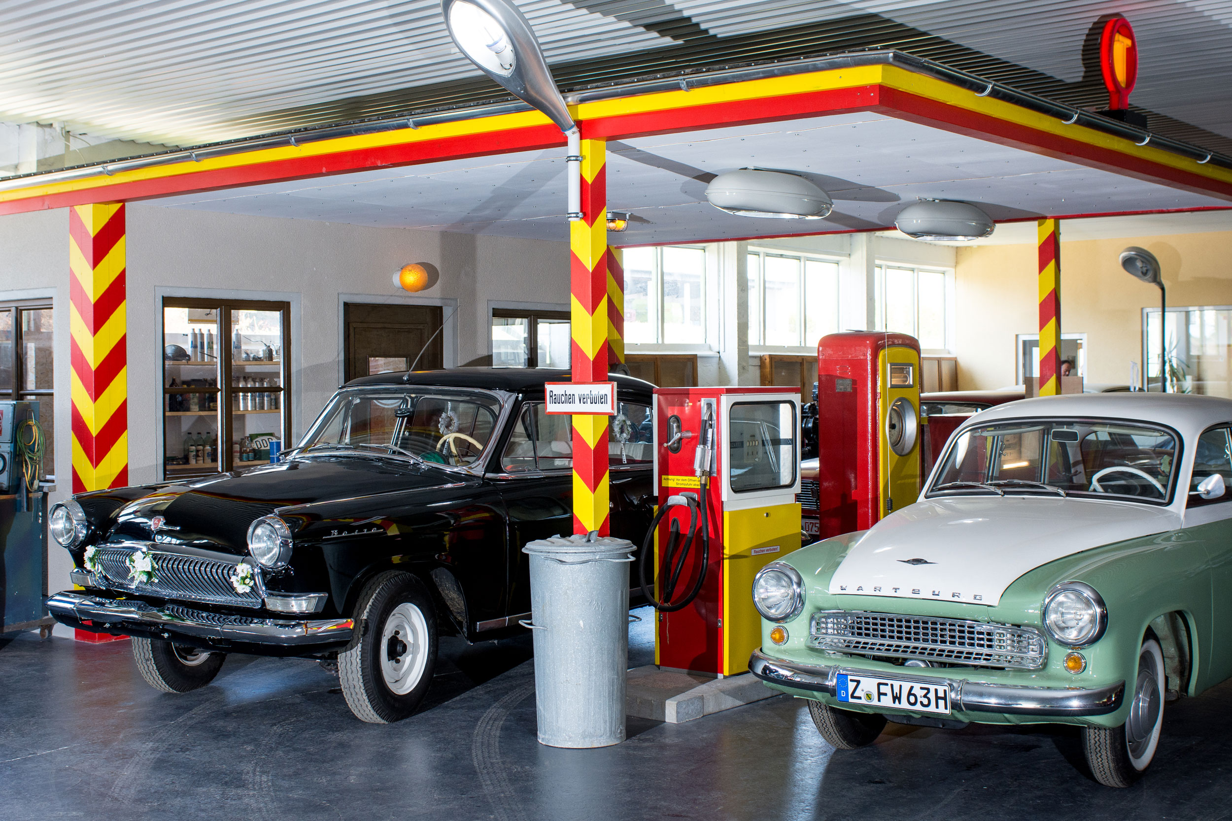 Original-Tankstelle Alte Tankstelle im Oldtimer-Museum mit einem schwarzen und einem weiß-cremefarbenen Oldtimer davor