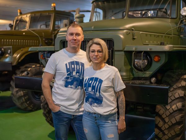 Frau und Mann vor Ural im Museum, beide tragen grau meliertes T-Shirt mit dunkelblauem Ural-Print und dunkelblauer Aufschrift URAL in kyrillisch
